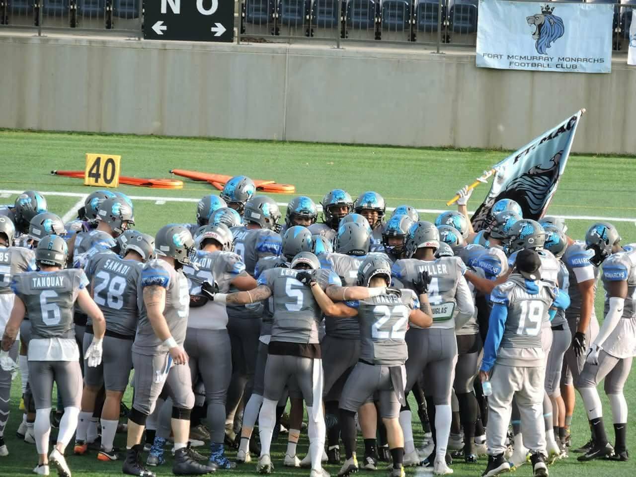 Monarchs team huddle with team flag raised on the field